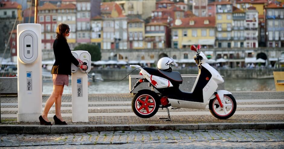 Vrouw laadt elektrische bromfiets op aan laadpaal